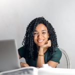 Happy ethnic woman sitting at table with laptop